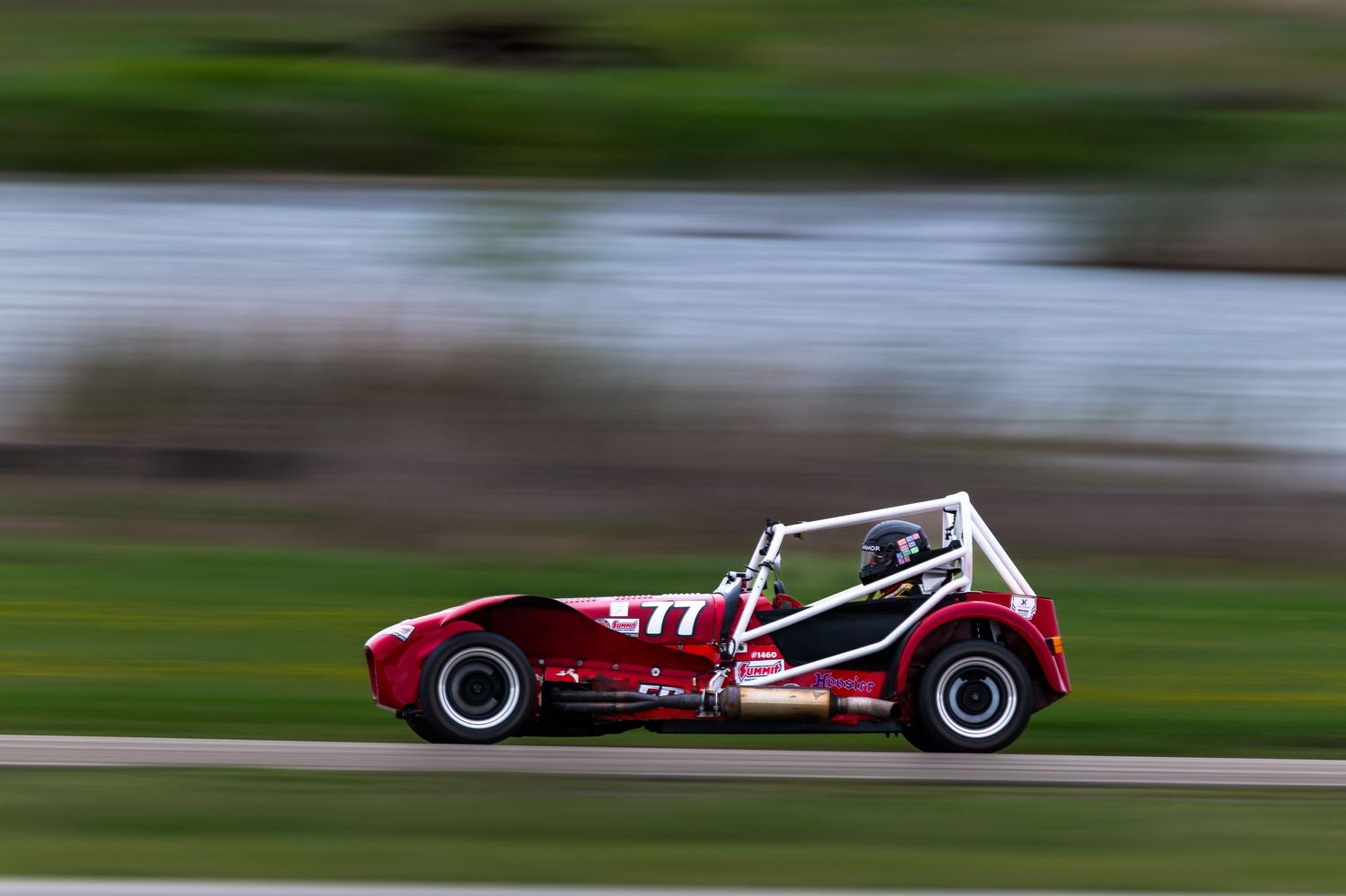 Red vintage Caterham Seven race car number 77speeding along a racing circuit.