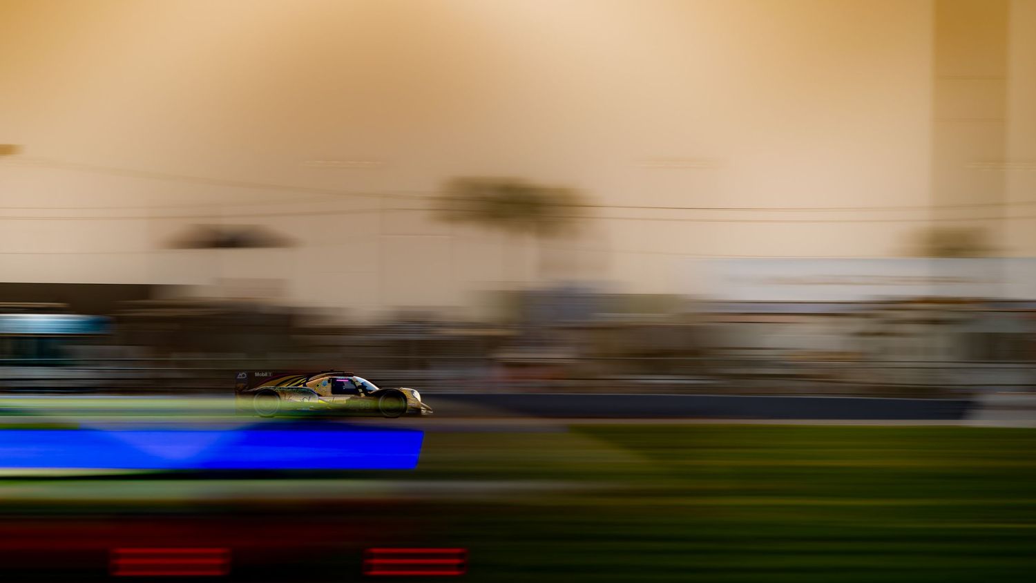Racing car blurs past grandstand at dusk on circuit.