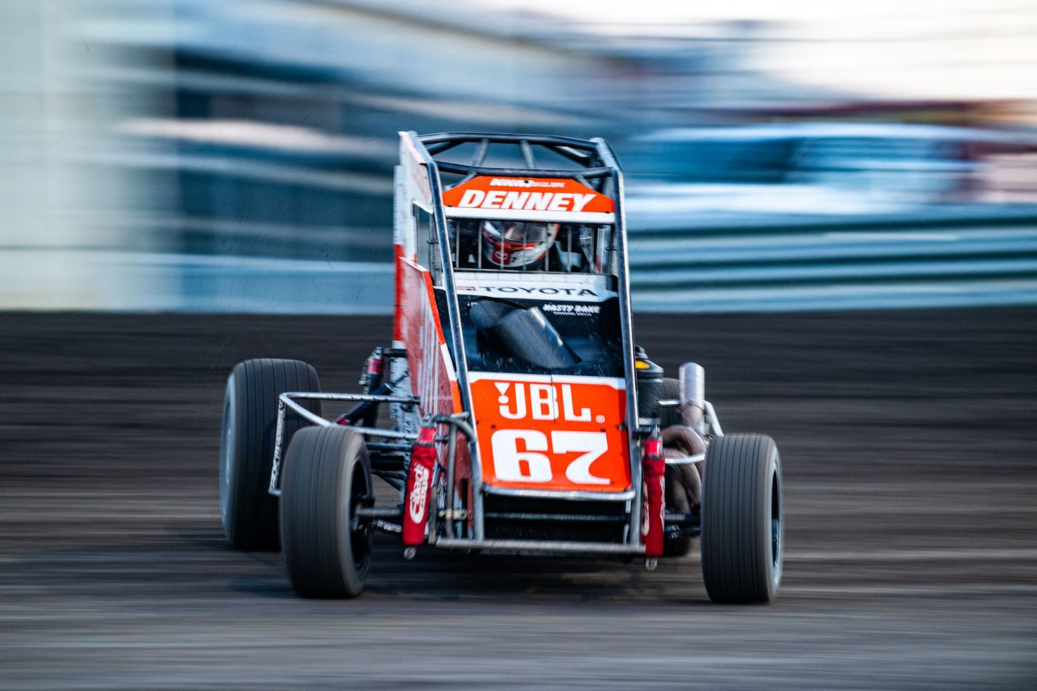 Orange JBL sprint car number 62 driven by Denney racing on a dirt oval track.