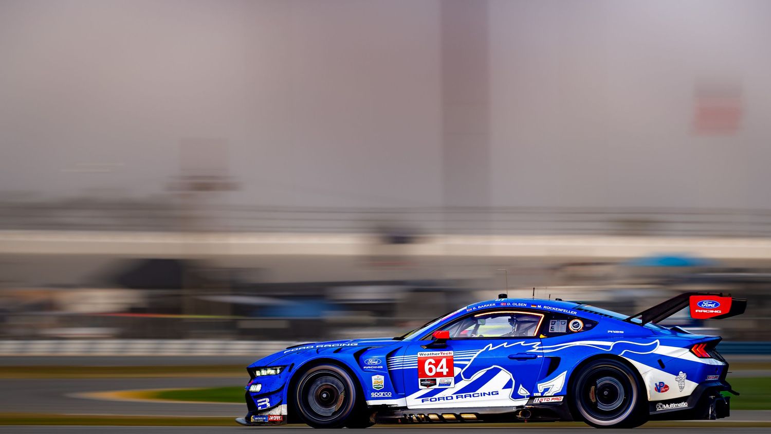 Blue Ford Mustang GT4 number 64 races on foggy track.