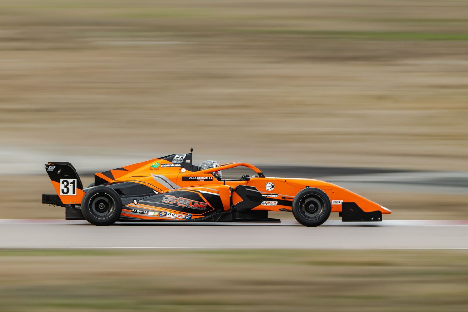 Orange formula car number 37 speeds along racing circuit track.