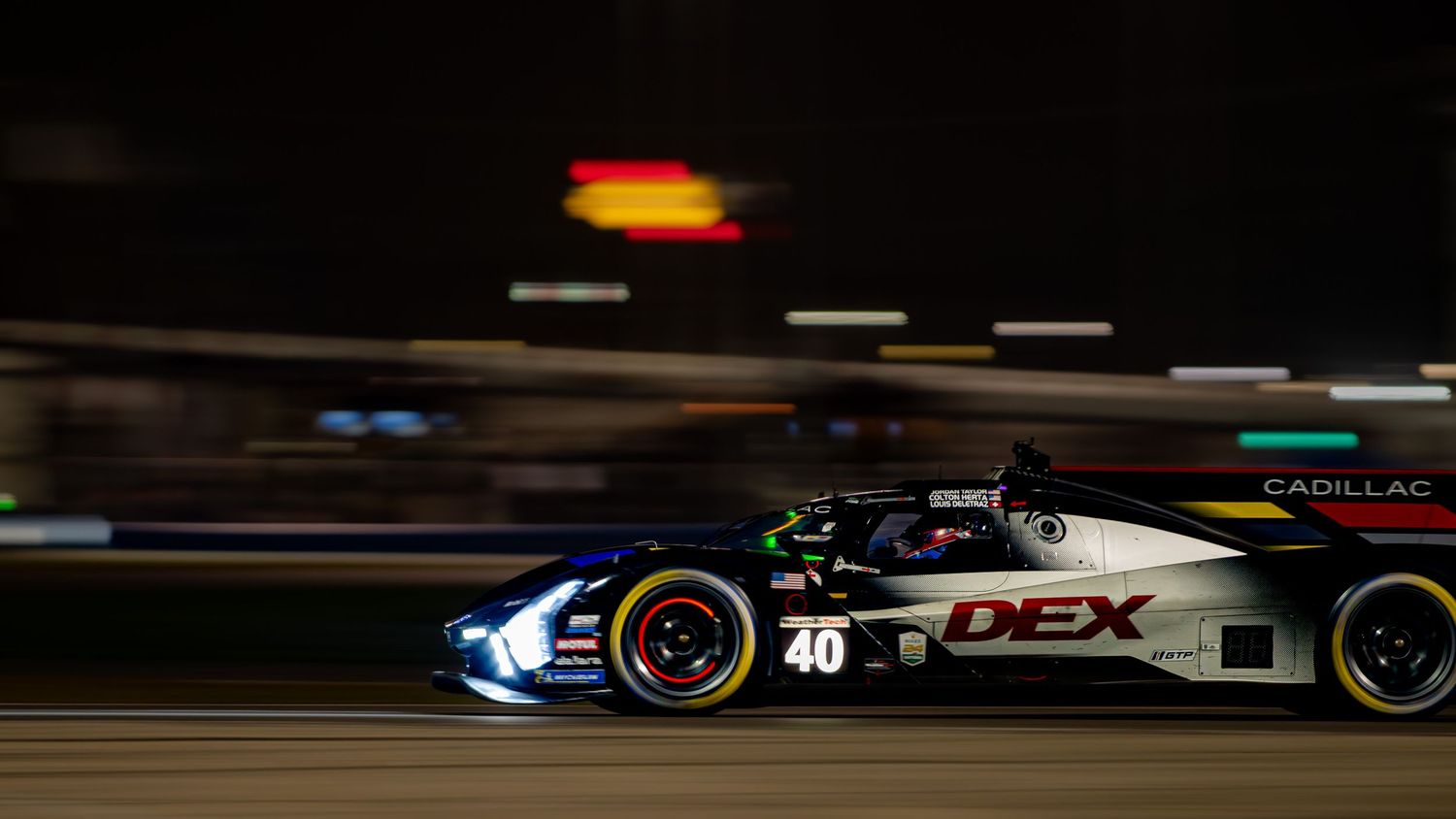 Cadillac DEX prototype race car number 40 speeding on track under night lights.