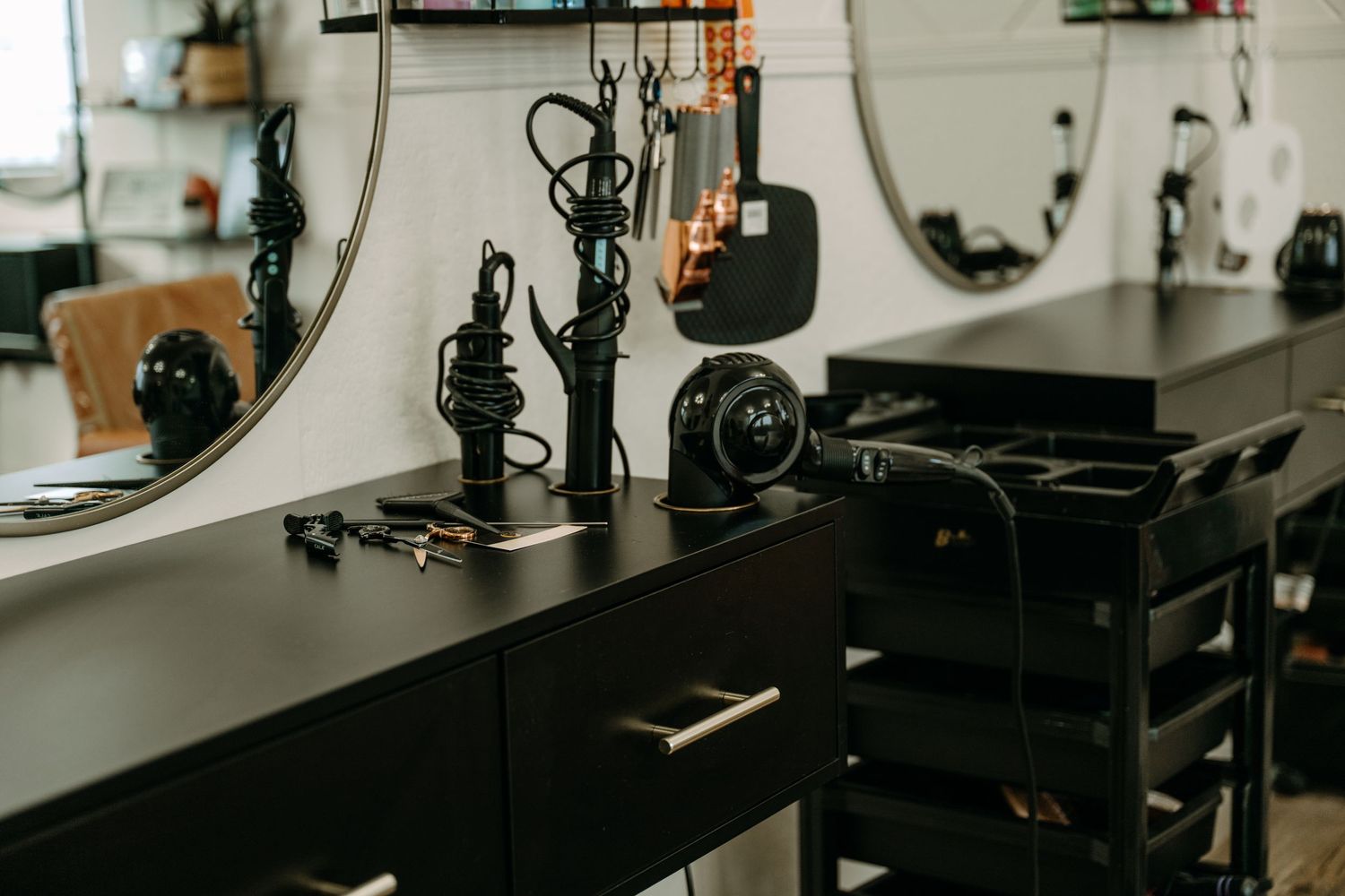 Modern black salon styling station with professional hair tools and round mirror.