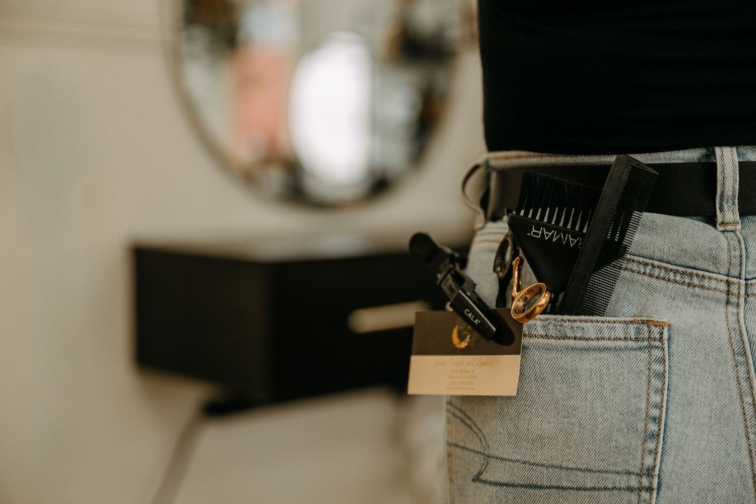 Close-up of hairstylist's jeans pocket with scissors and clips tucked inside.