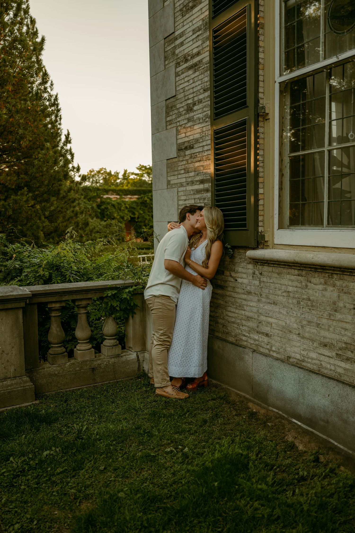 Couple sharing a kiss against historic stone building exterior at dusk.