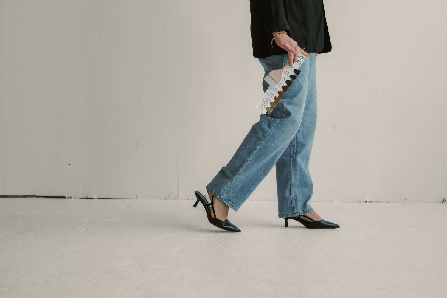 Woman in blue jeans and black heels walking while carrying a beaded phone charm accessory.
