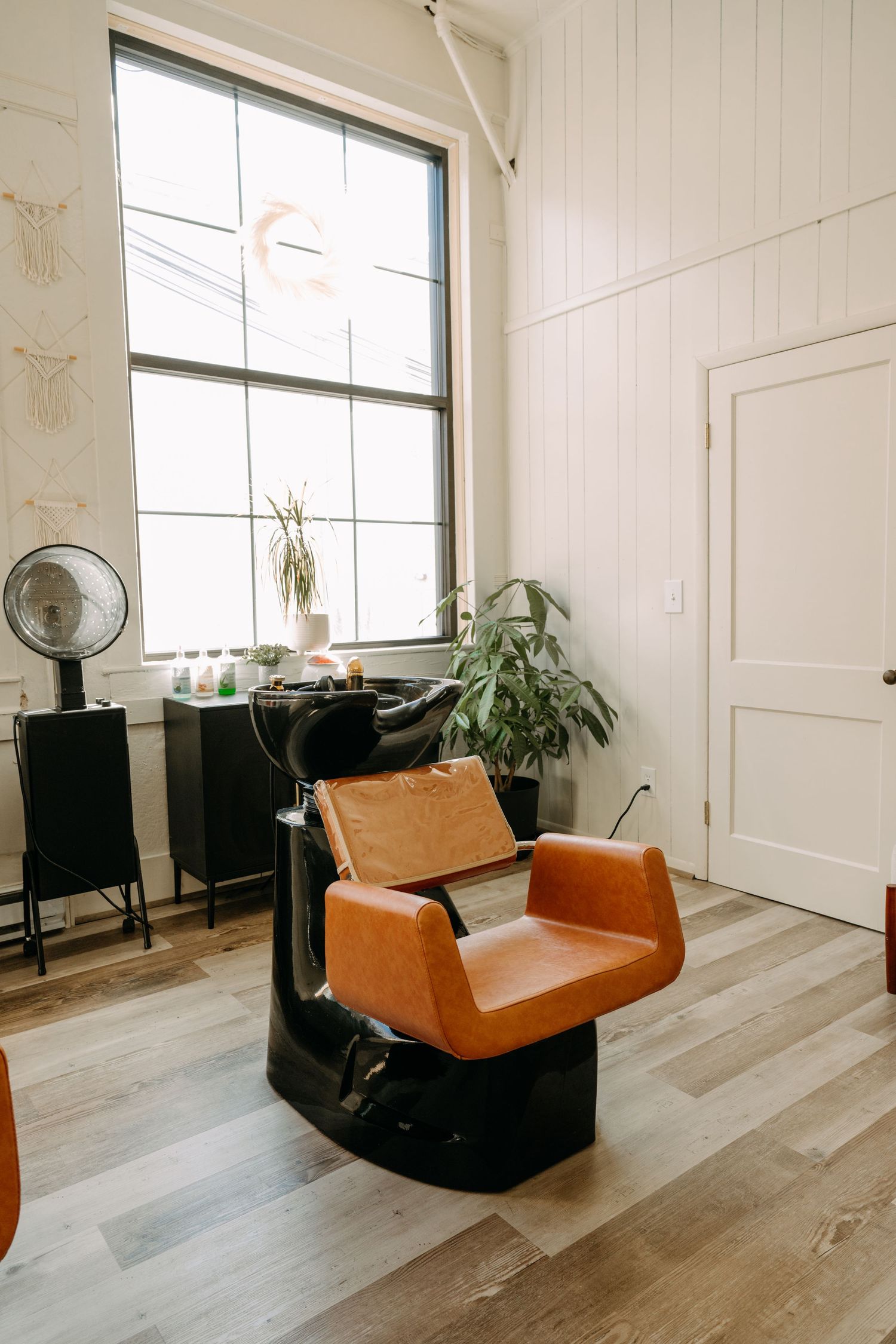 Retro orange leather salon shampoo chair beside a large window in a bright, modern hair salon with wood floors.