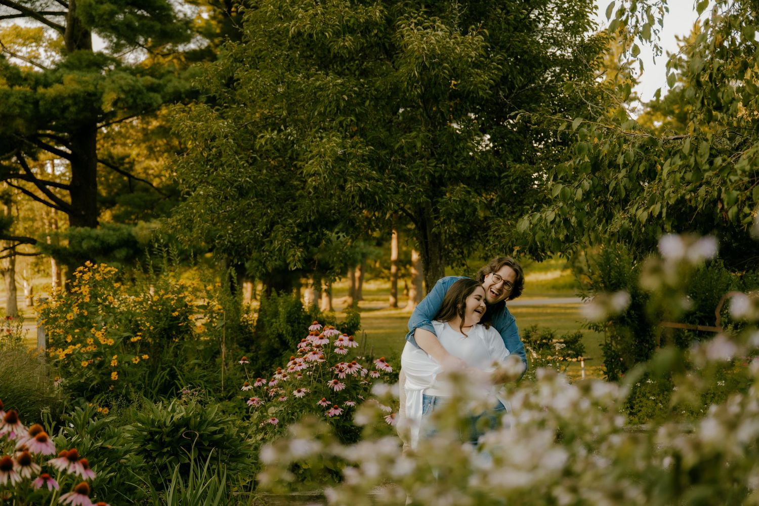 Couple embracing in a beautiful garden surrounded by colorful flowers and lush green trees.