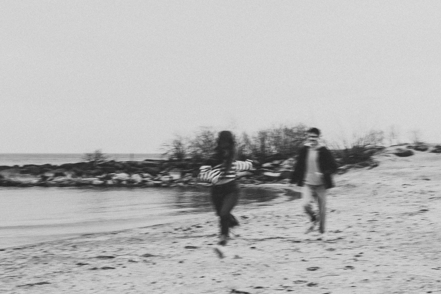 Black and white photo of a couple running and holding hands on a beach shoreline.