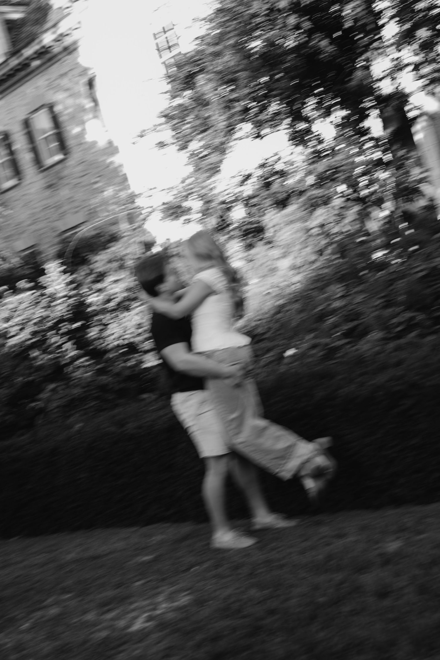 Black and white blurred photo of a couple kissing outdoors near a historic building.