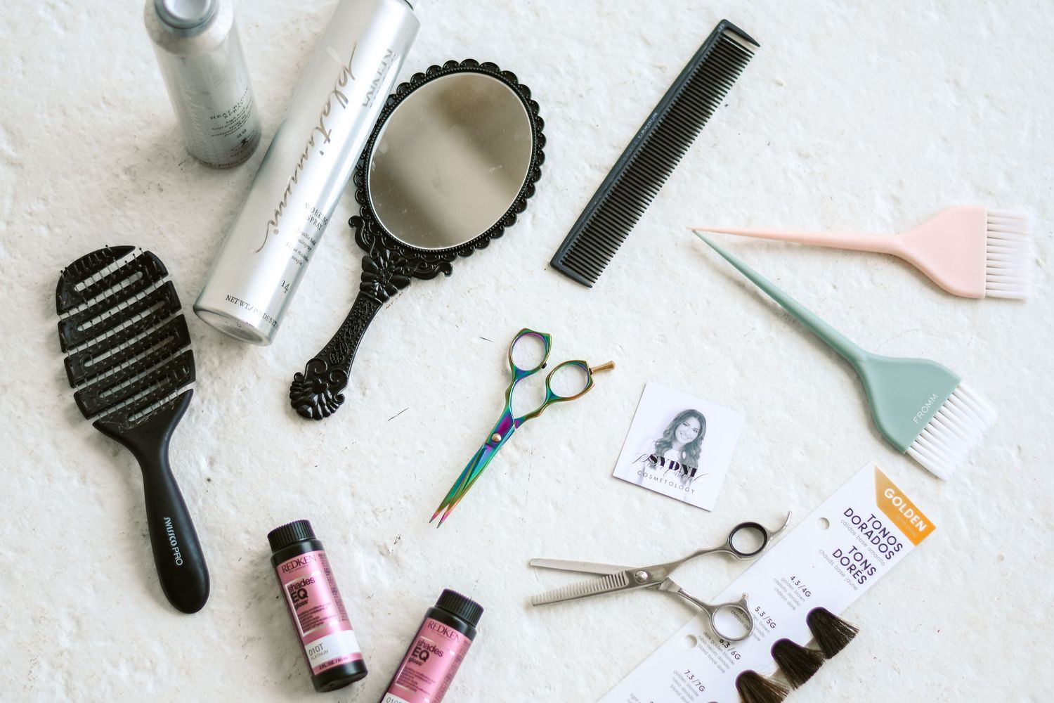 Flat lay of professional hair styling tools including scissors, brushes, mirror, and hair products.