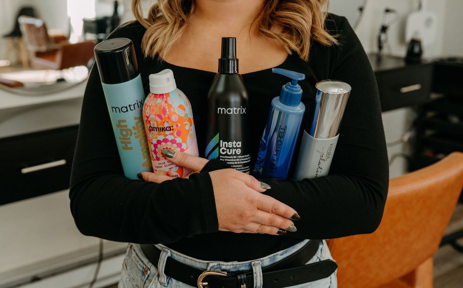 Woman in black top holding multiple Matrix hair care products in a salon setting.