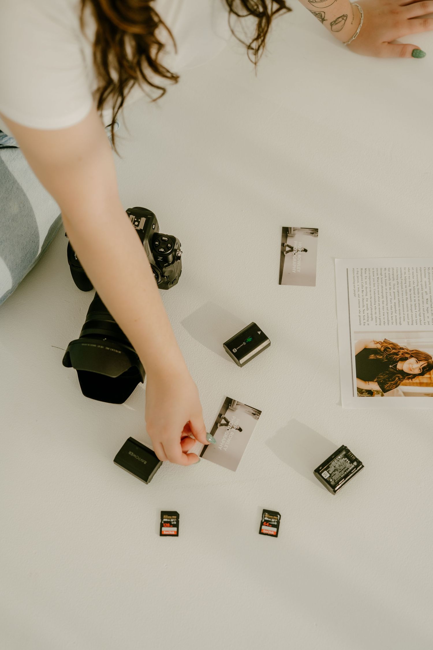 Overhead view of photographer reviewing printed photos with camera and memory cards on white floor.