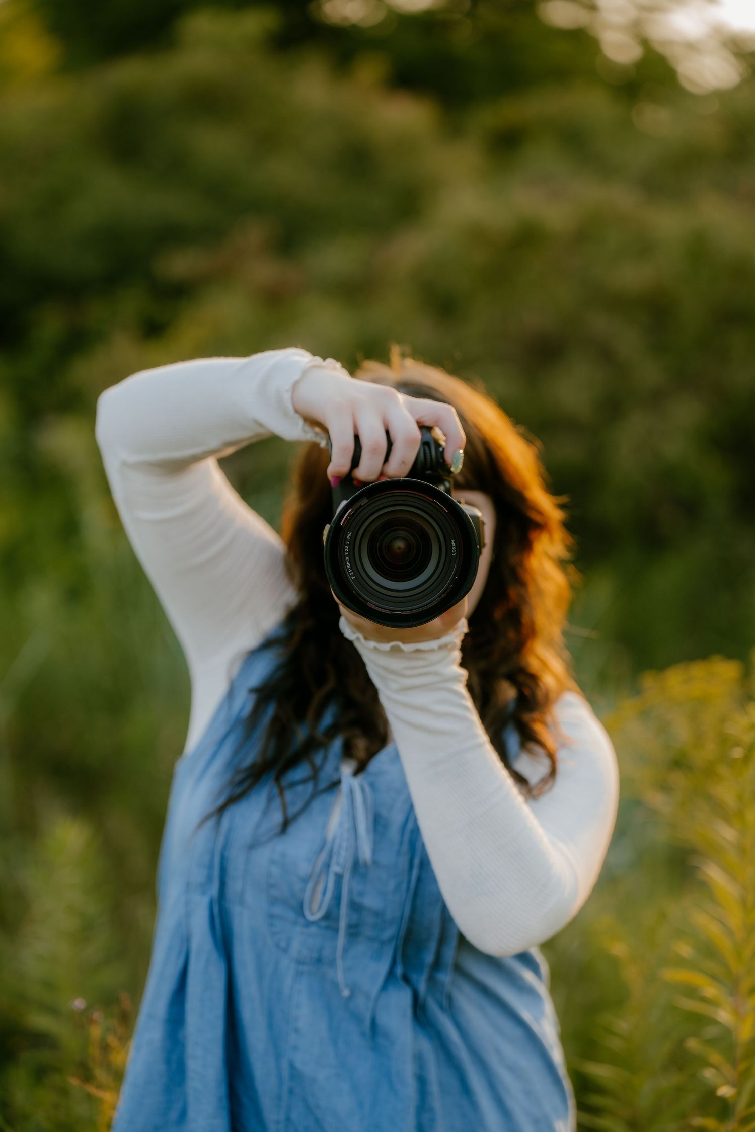 Female photographer raising a DSLR camera to her face outdoors during golden hour.