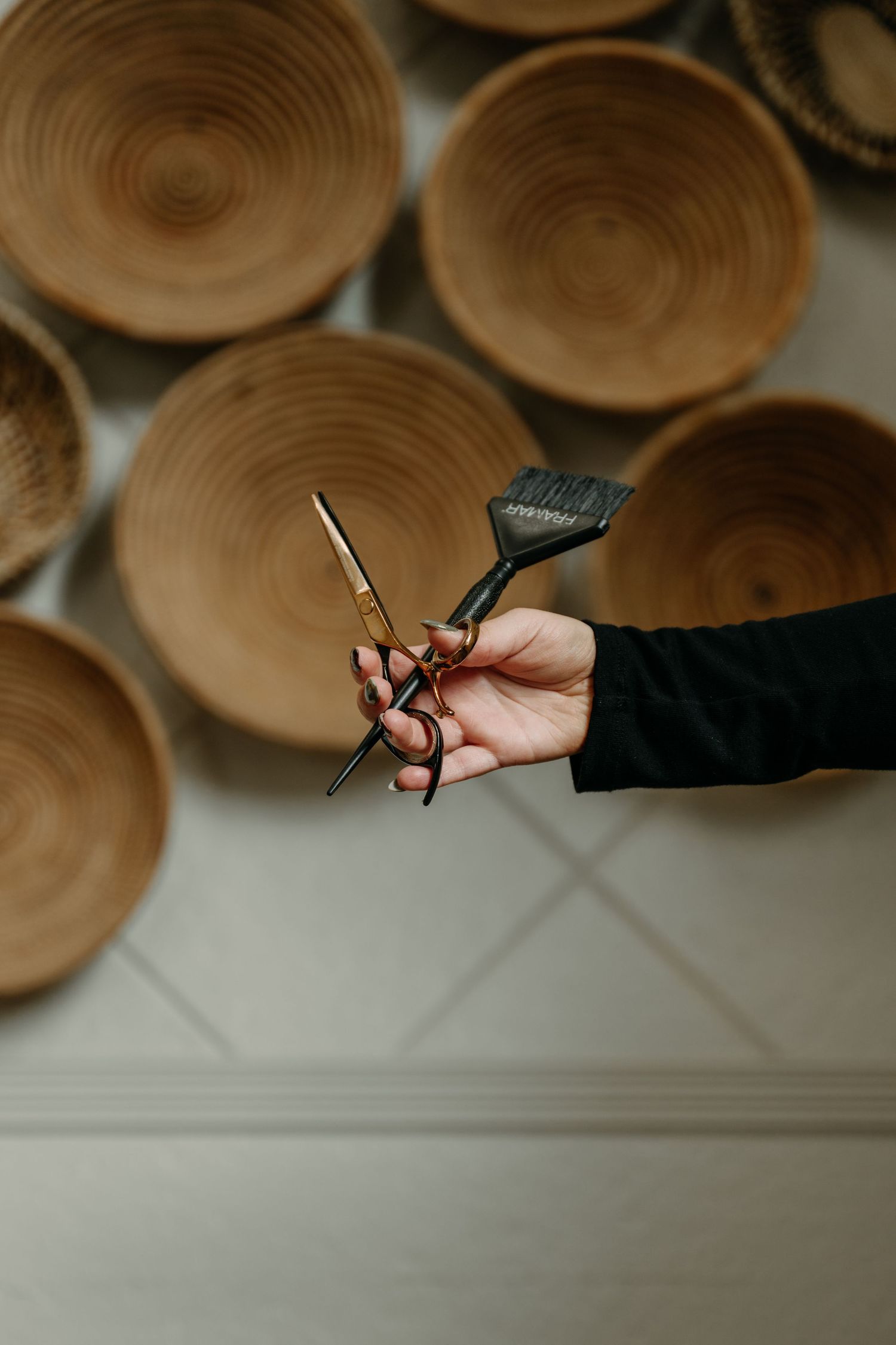 Hand holding gold scissors and color brush in front of decorative wooden bowls.