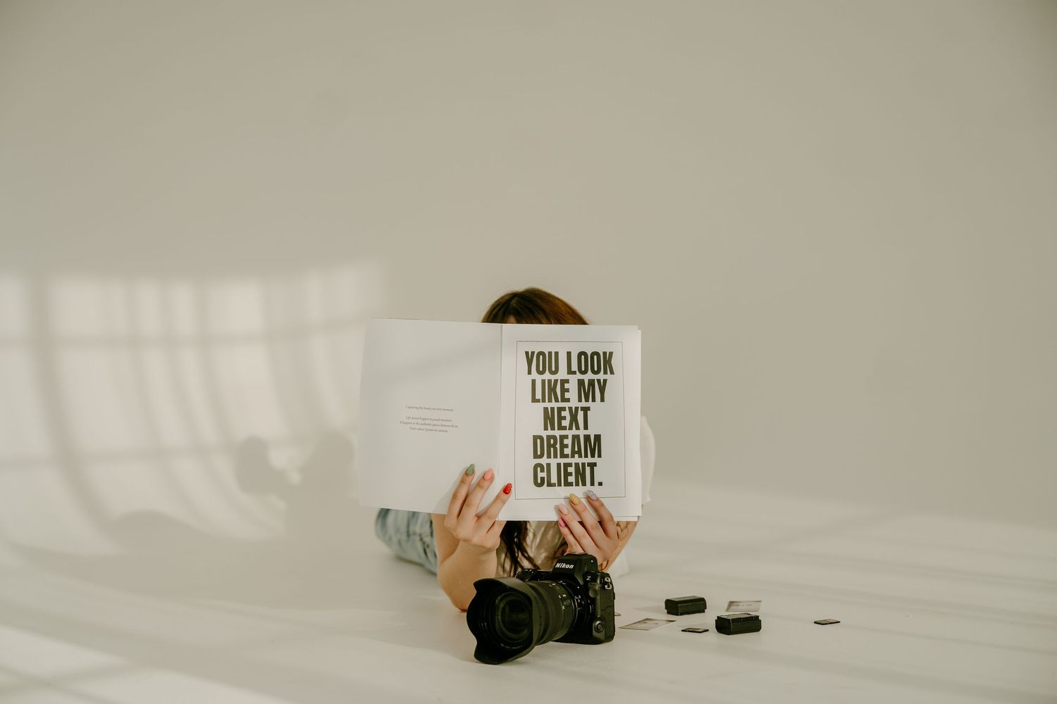 Photographer lying down holding a sign reading You Look Like My Next Dream Client with camera nearby.
