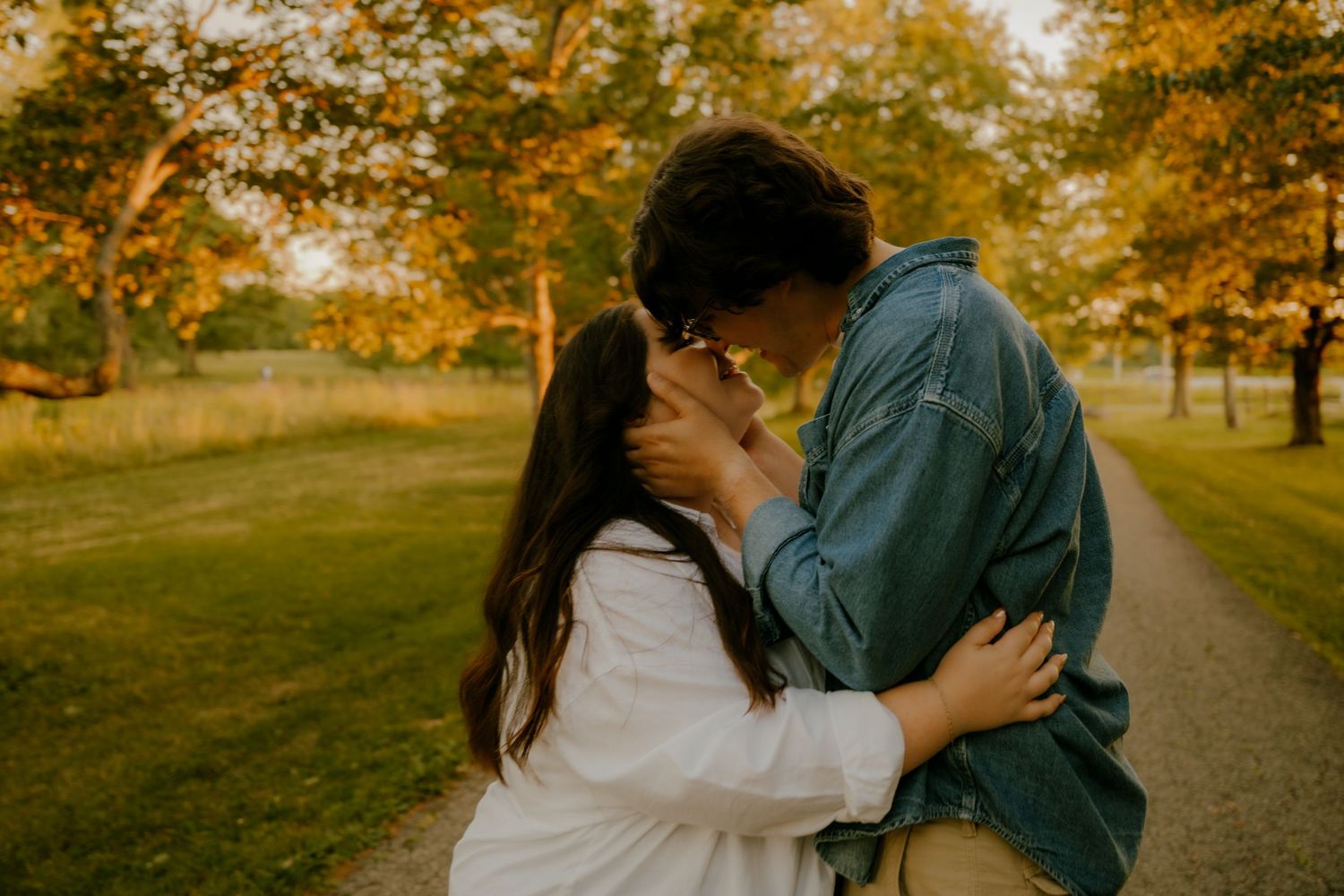 Young couple sharing a tender moment kissing on a tree-lined path during golden autumn sunset.