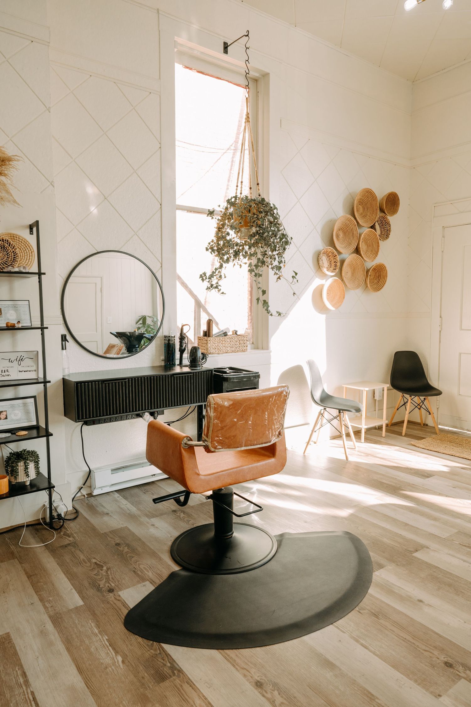 Bright modern hair salon interior with leather styling chair, round mirror, and boho wall decor.