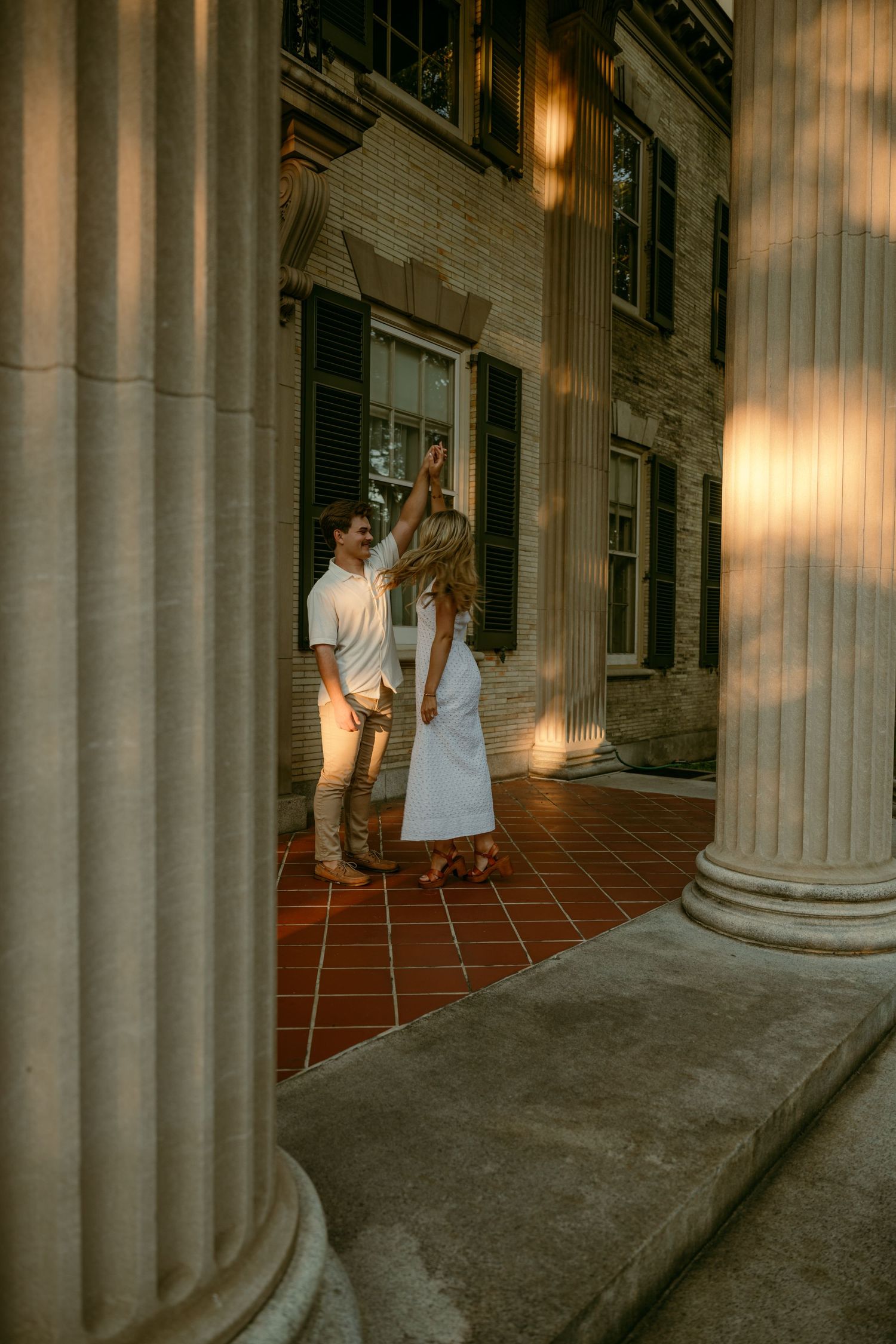 Couple dancing between elegant stone columns of a historic building in warm golden light.