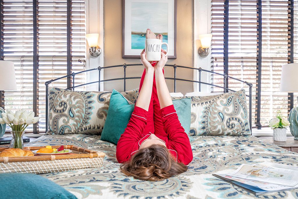 Woman lounging on a bed holding a coffee mug in the bedroom of a Savannah vacation rental
