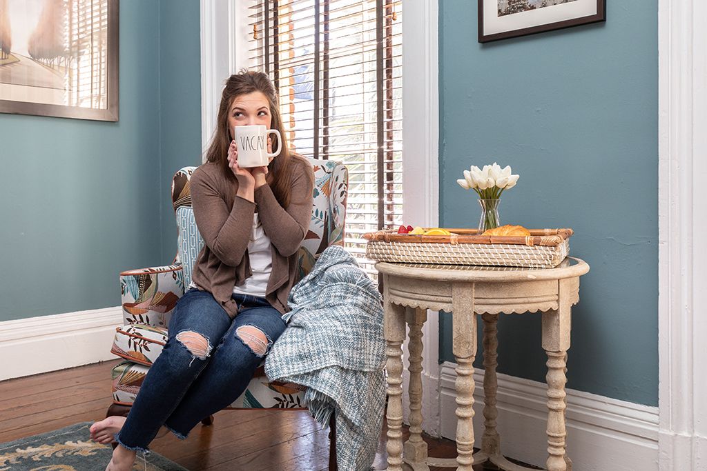 Woman drinking coffee in an armchair with a breakfast tray in a Savannah vacation rental