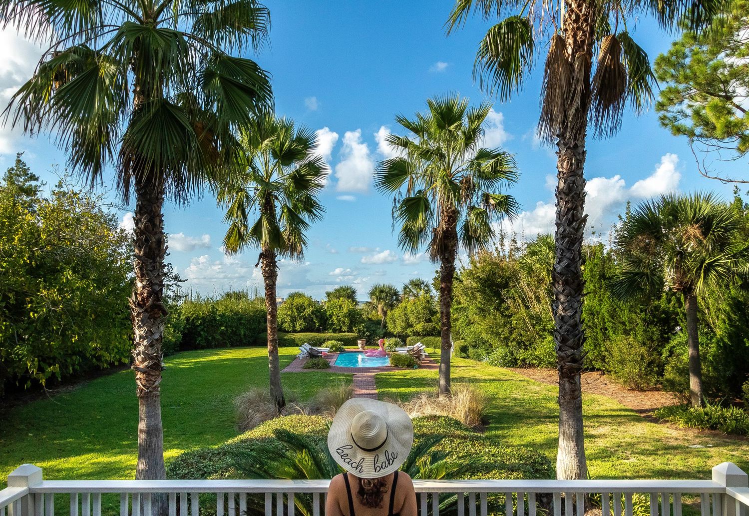 Woman in a sun hat on a deck overlooking a palm tree-lined yard and pool at a Tybee Island vacation rental