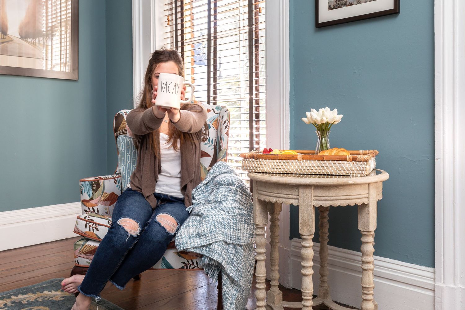 Woman drinking coffee in an armchair with a breakfast tray in a Savannah vacation rental