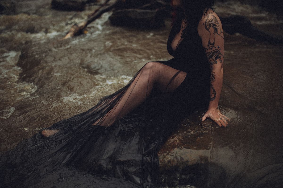 A person in a flowing black dress poses dramatically on a rocky terrain in a river near Spartanburg, South Carolina.