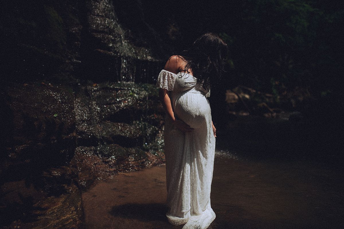 Moody maternity boudoir portrait of a woman standing in front of a waterfall near Greenville, South Carolina.