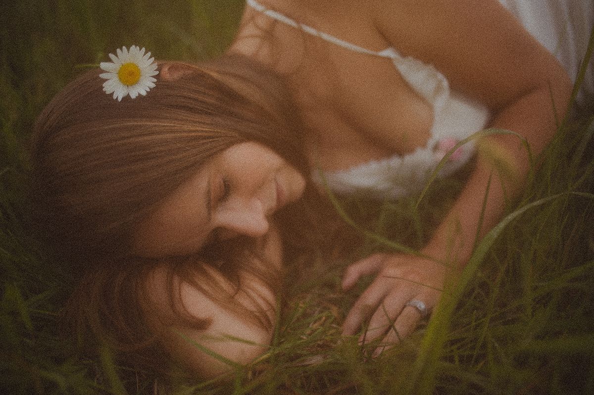 A person lies in a meadow with white daisies, creating a dreamy outdoor boudoir portrait in soft natural lighting in Spartanburg, SC..