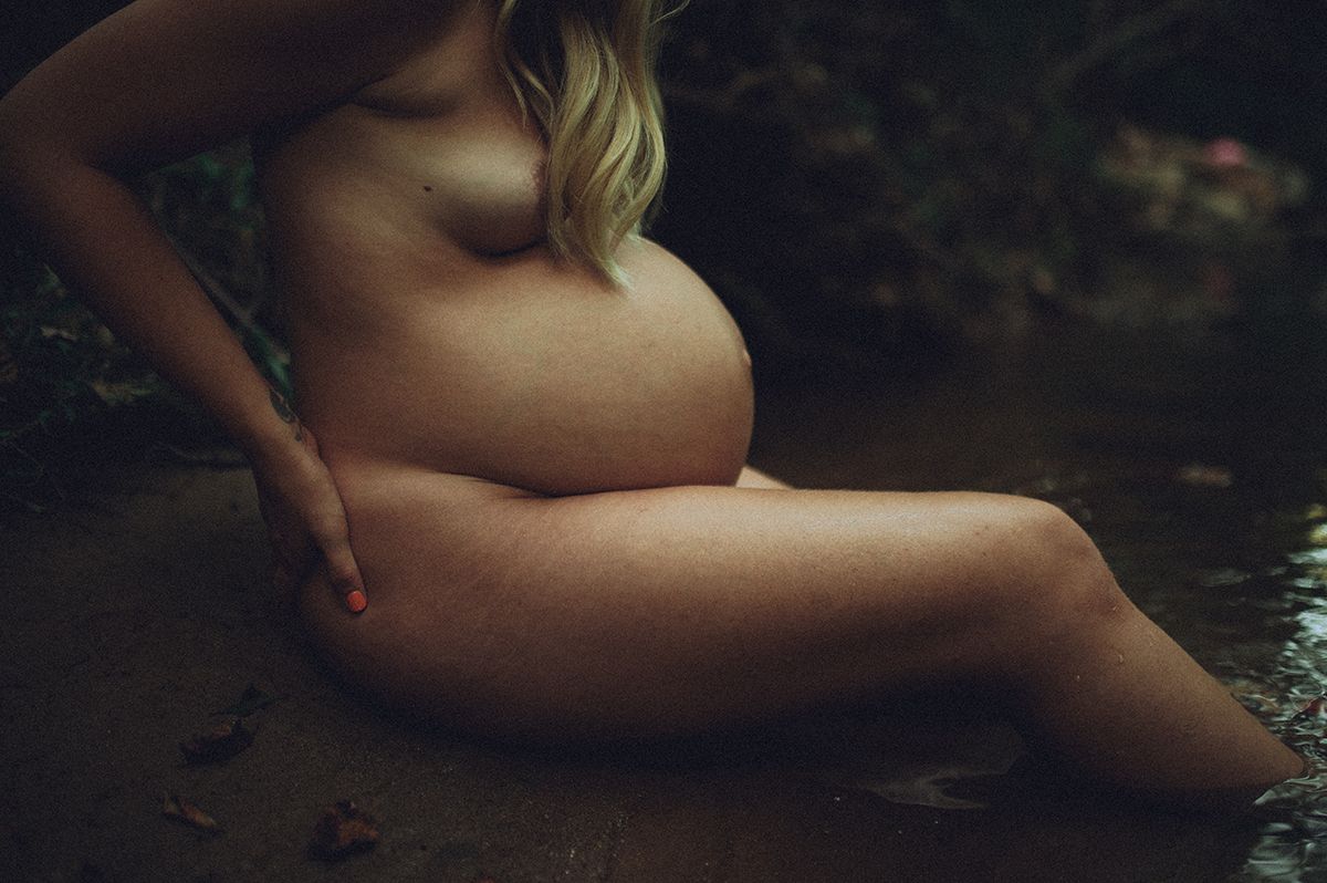 Artistic maternity boudoir photo showing a pregnant silhouette reclining in moody natural lighting in North Carolina forest.