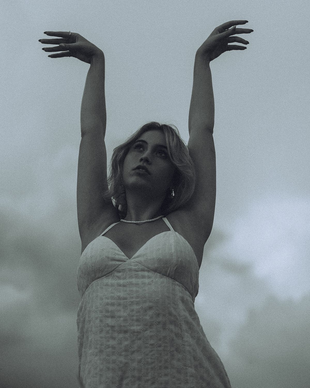 A moody black and white portrait showing a person reaching upward against a cloudy sky in Spartanburg, South Carolina.