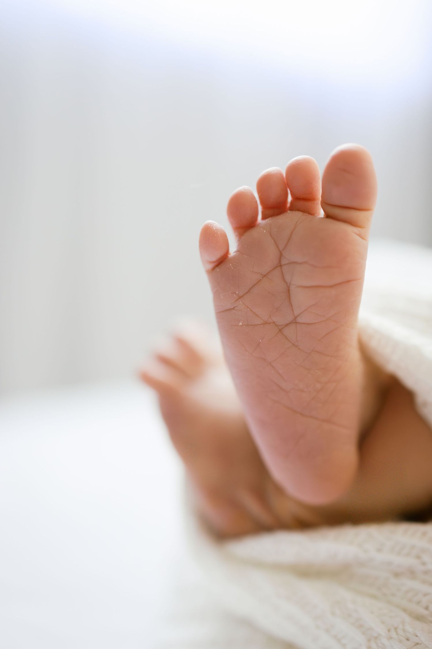 Close-up of a newborn baby's soft tiny foot with delicate skin texture, resting on a white blanket.