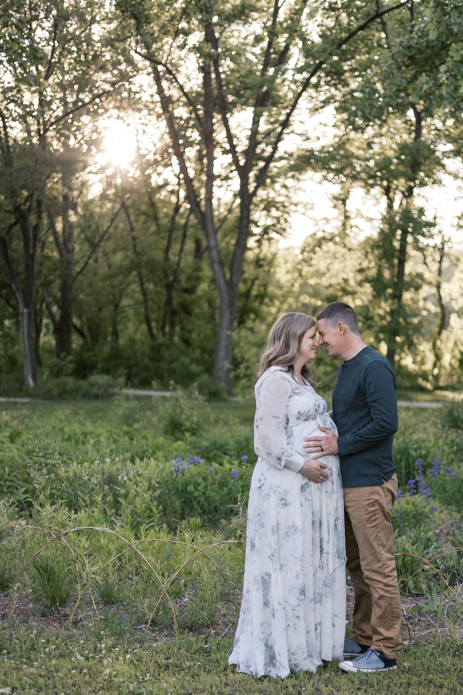 Couple sharing tender moment in sunlit field during outdoor maternity session by Katy Rose Photography.