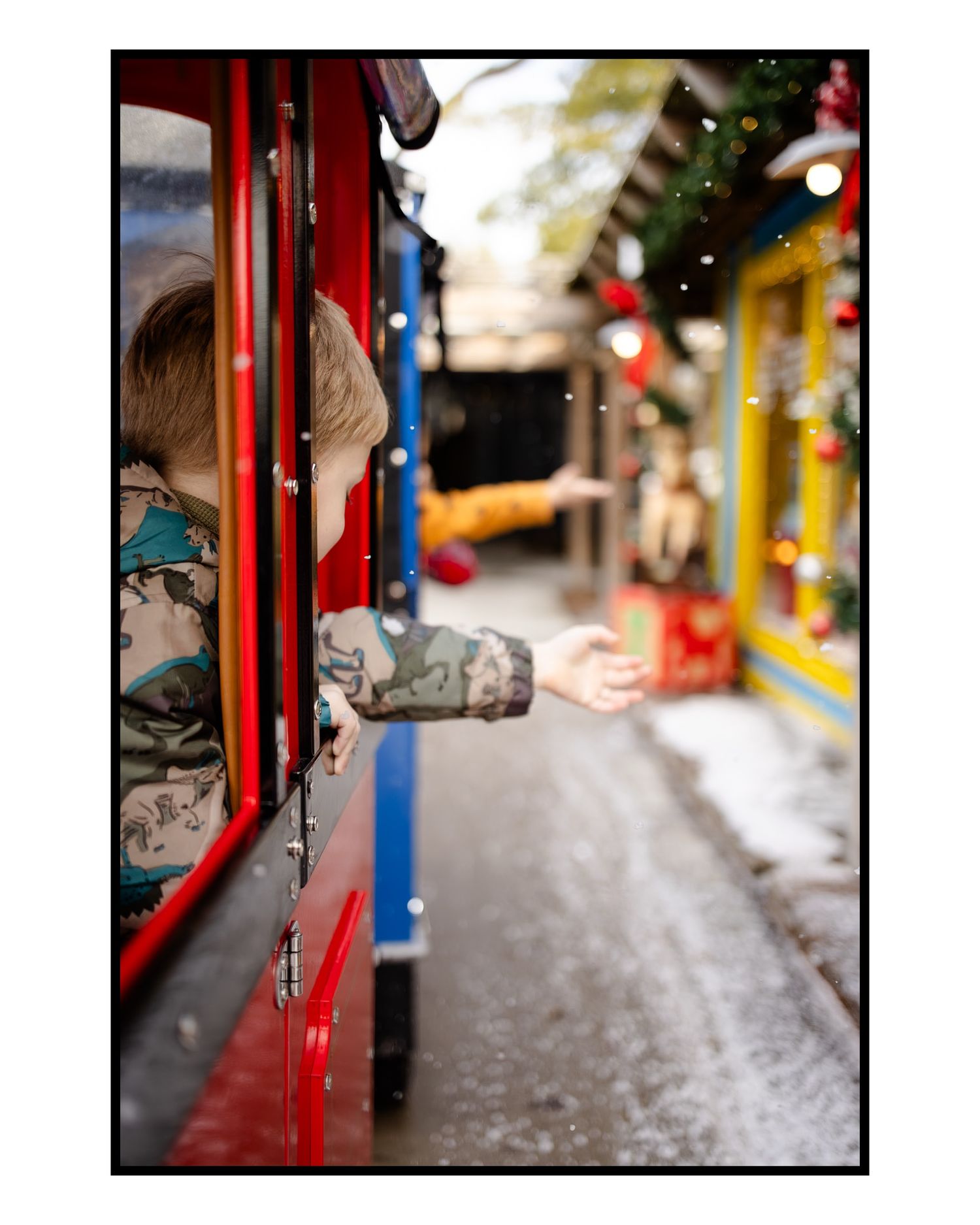 Red train car moving through a festively decorated street with blurred lights for fun Christmas Session in Indianapolis, Indiana.