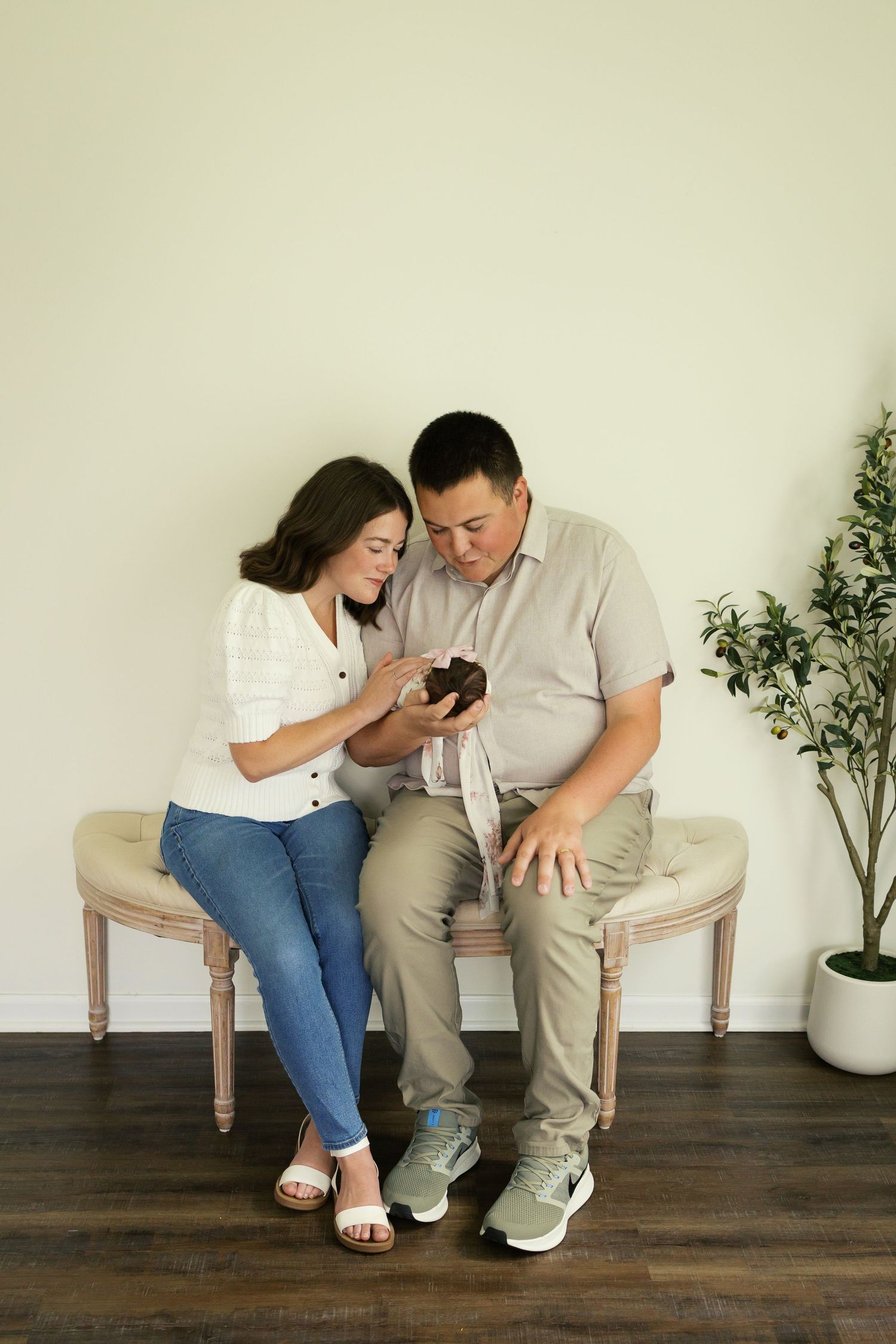 A couple sits on a bench looking at a smartphone together in a bright, modern room with a potted plant nearby.