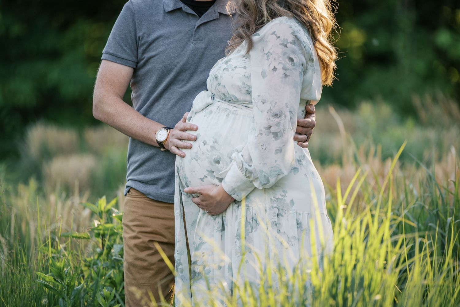 Pregnant couple with man's hand on baby bump in a grassy field at sunset for Indianapolis Maternity Session by Katy Rose Photography