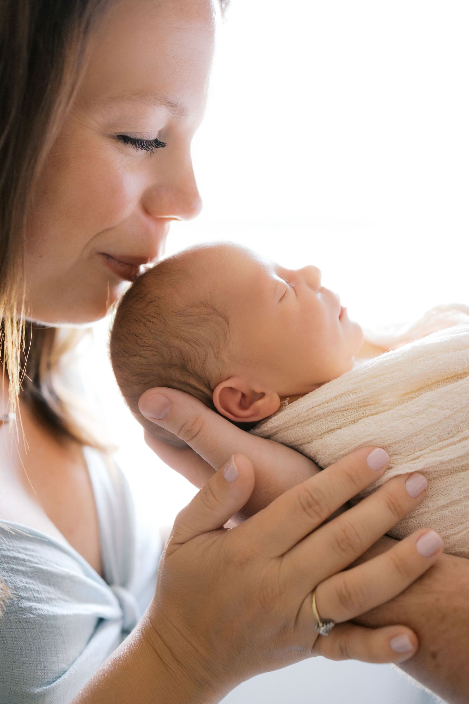 Mother kisses her sleeping newborn in a soft blanket, cradled gently in her hands during Brownsburg Newborn Session by Katy Rose Photography
