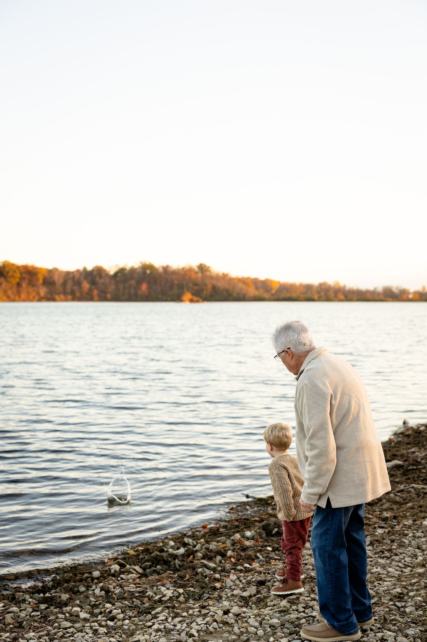 Grandpa and grandson spending quality time throwing rocks in the water at Eagle Creek State Park during family session in Indianapolis, IN