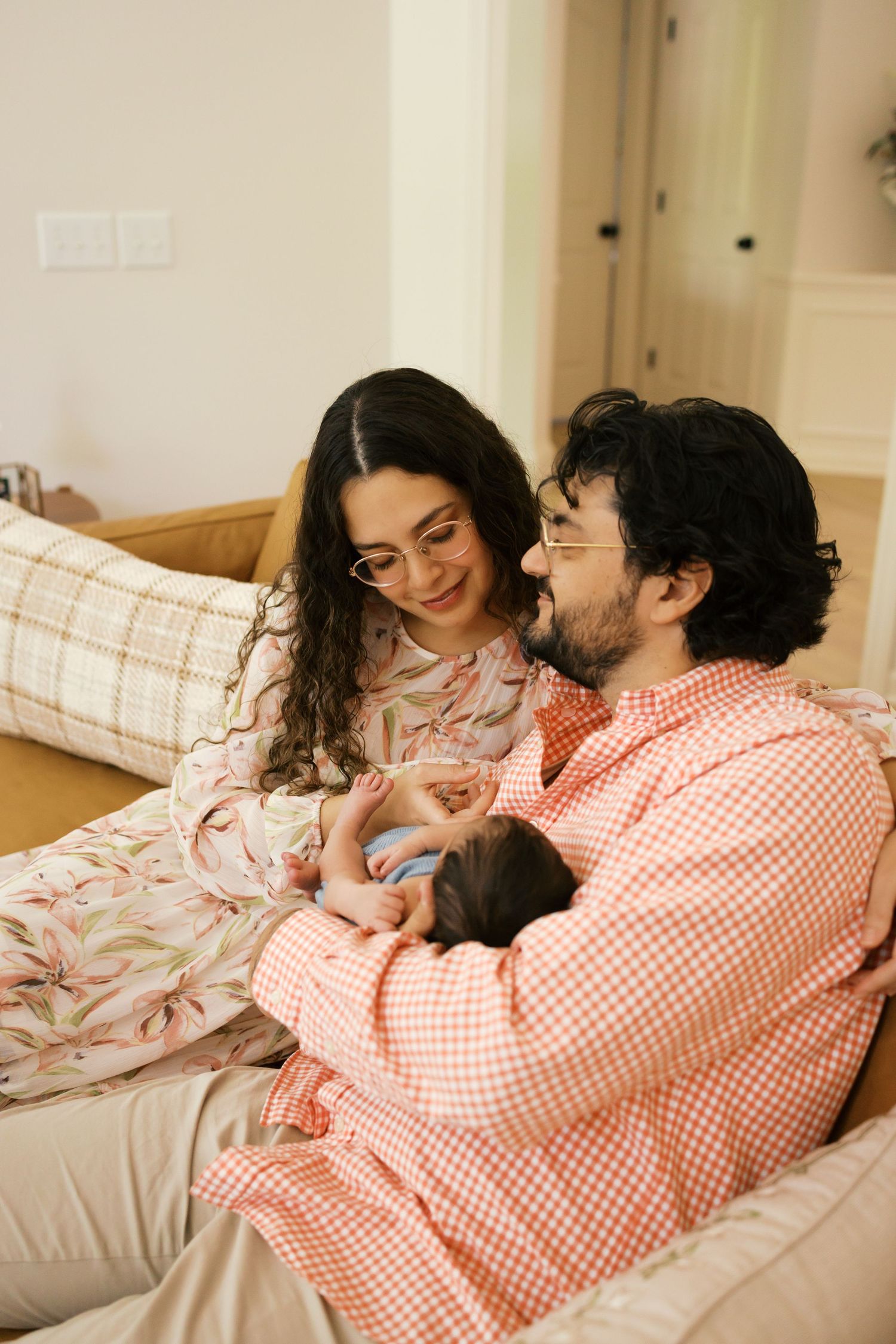 A couple sitting on a couch, smiling and holding their newborn baby during Noblesville, Indiana in-home newborn session