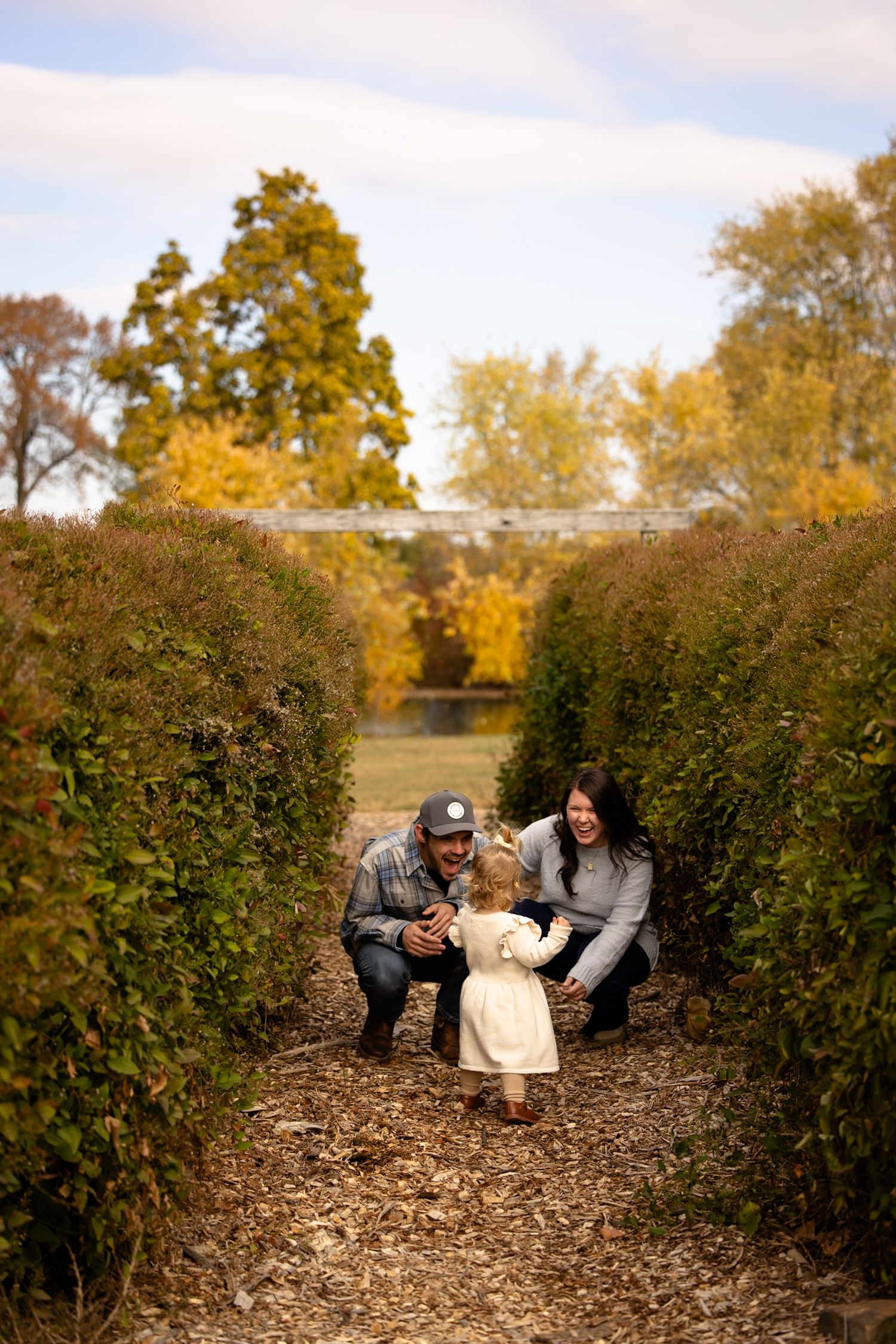 A family sits together on mulch surrounded by green hedges during a fall photo shoot in Hendricks County by Katy Rose Photography.