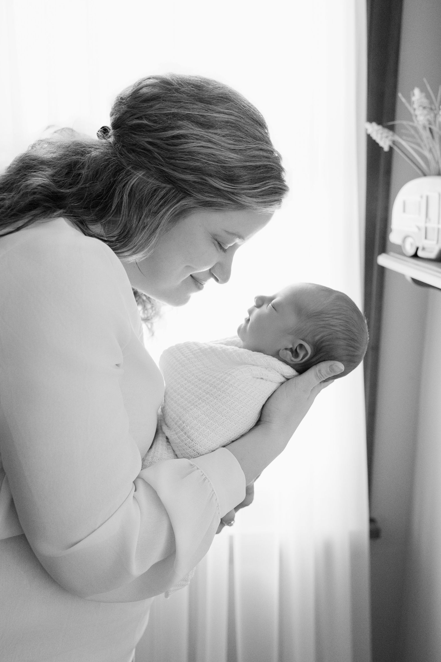Black and white photo of a mother tenderly gazing at her swaddled newborn baby cradled in her arms.