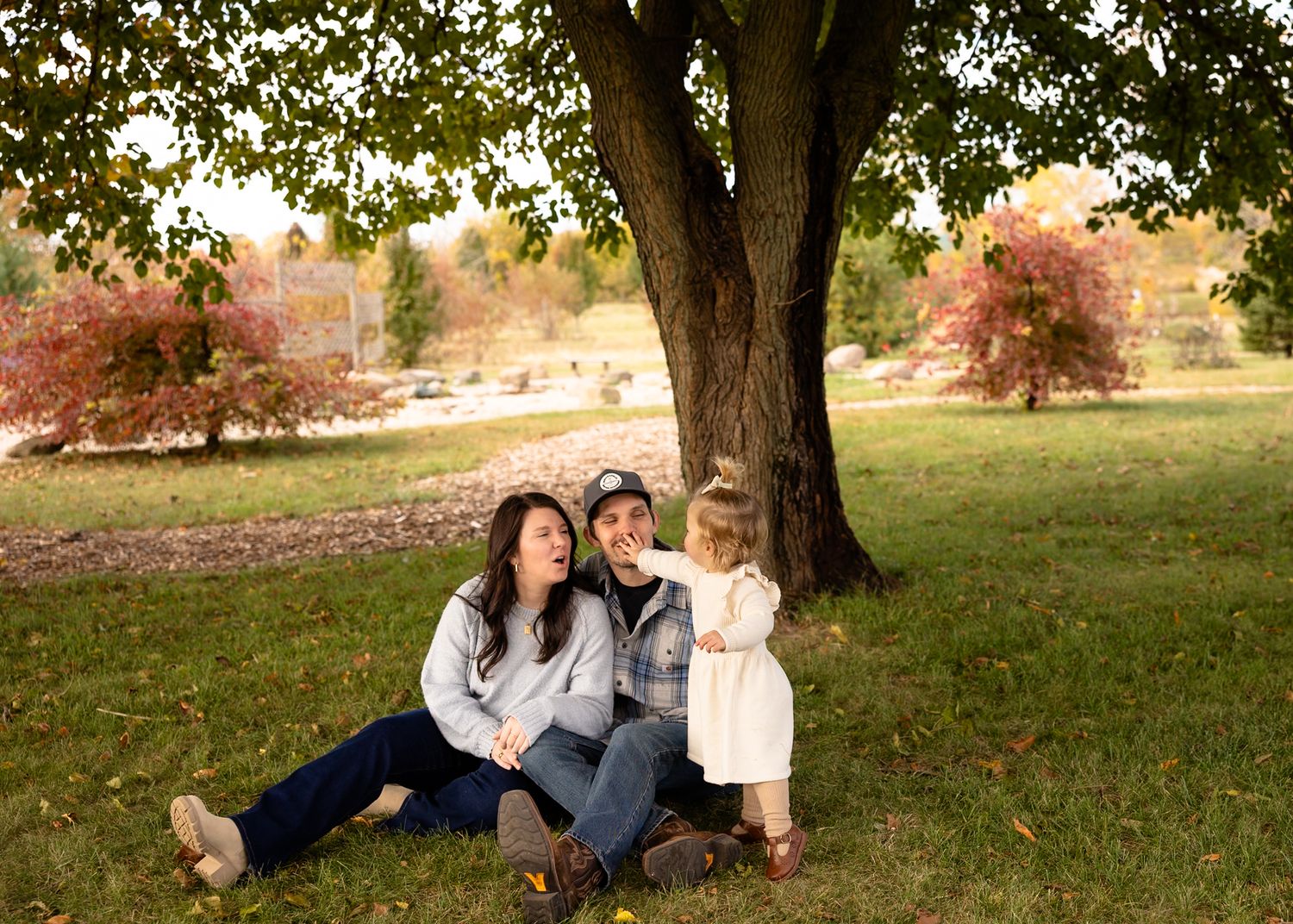 A family lounges together under an autumn tree on a grassy hillside during a family photo session in Brownsburg, Indiana.