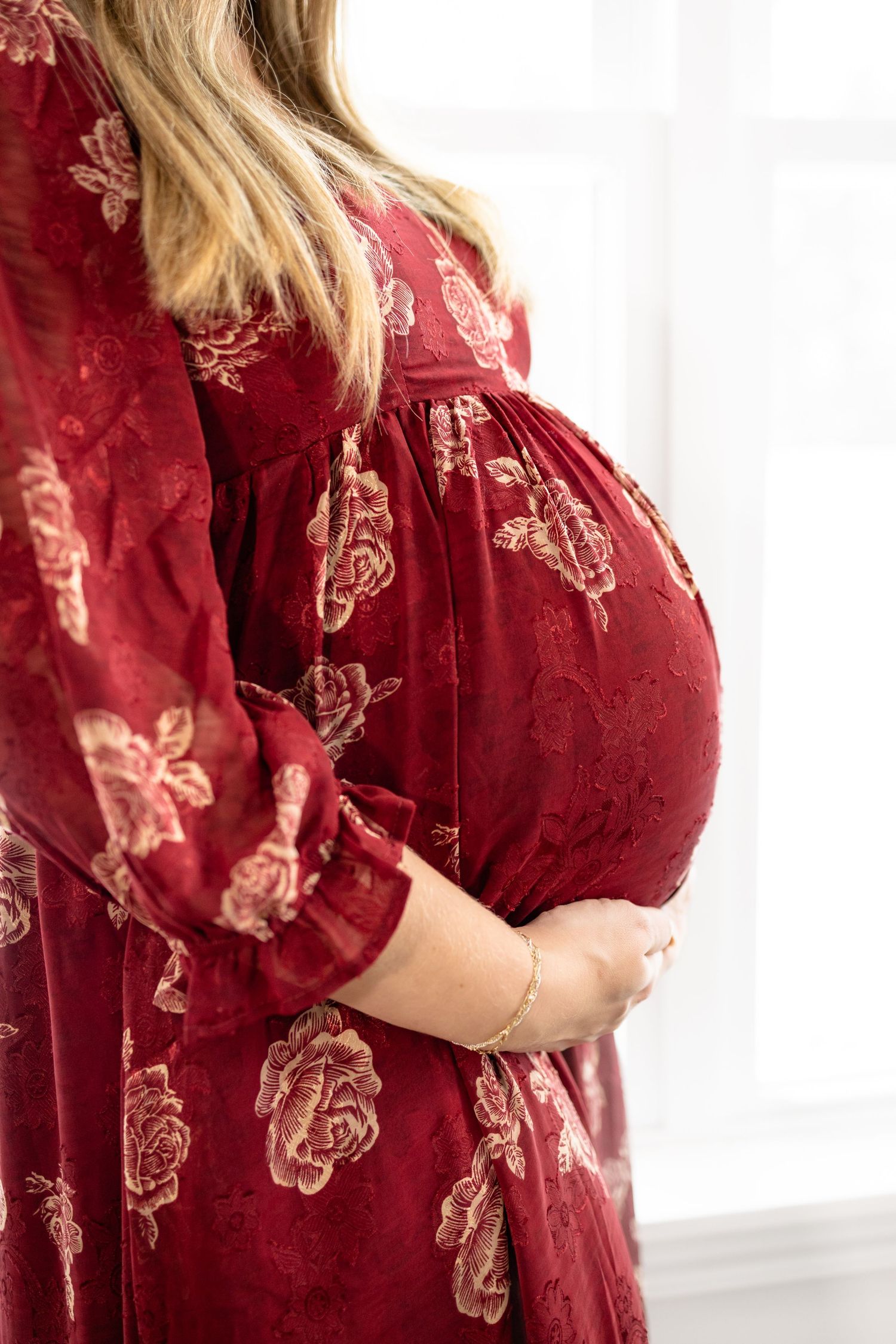 Side view of a burgundy floral maternity dress with delicate pattern details.