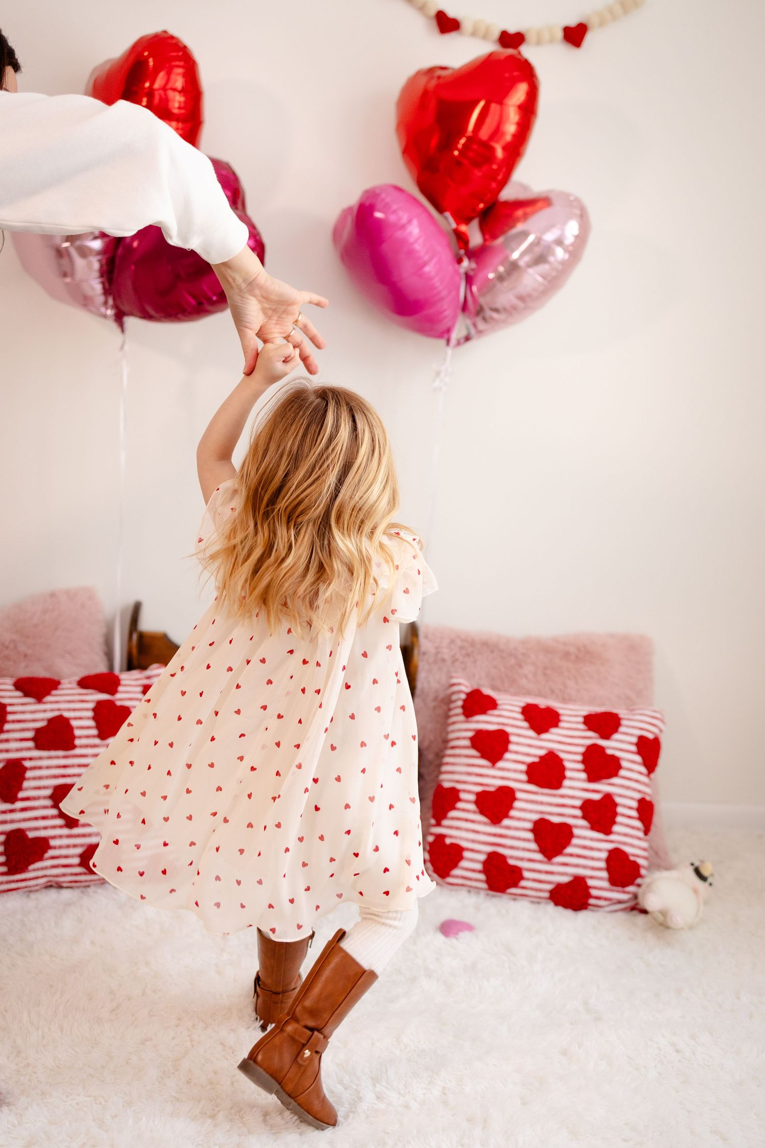 Child in polka dot dress dances with heart balloons and Valentine's Day presents in white studio setting for. Valentine's Day Minis