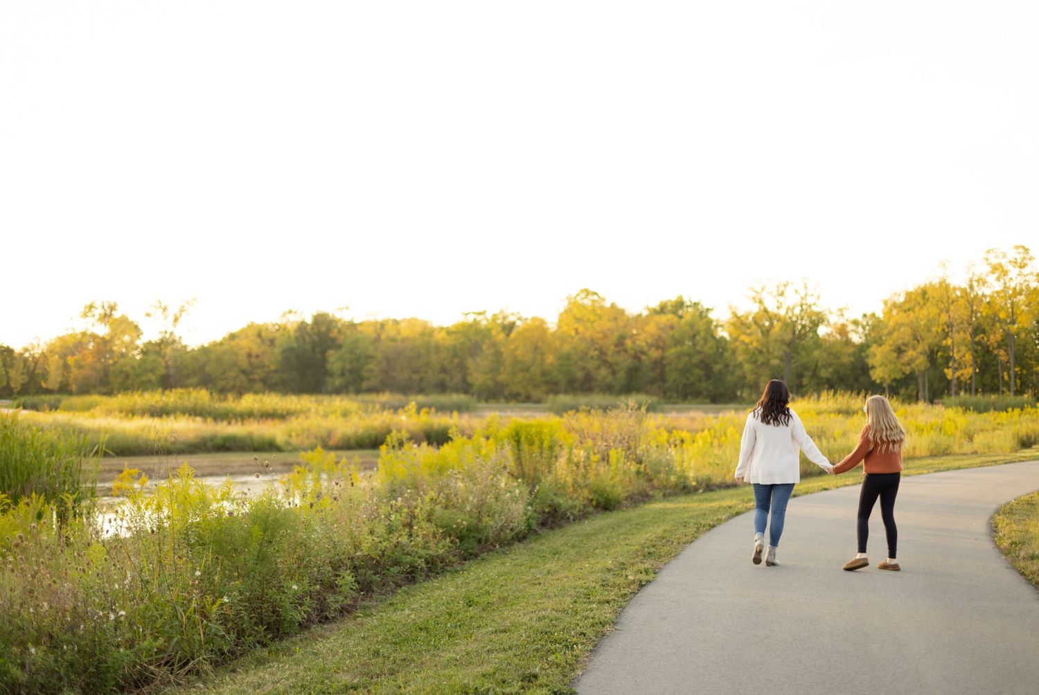 Two people walk along a nature path surrounded by golden wildflowers at sunset.