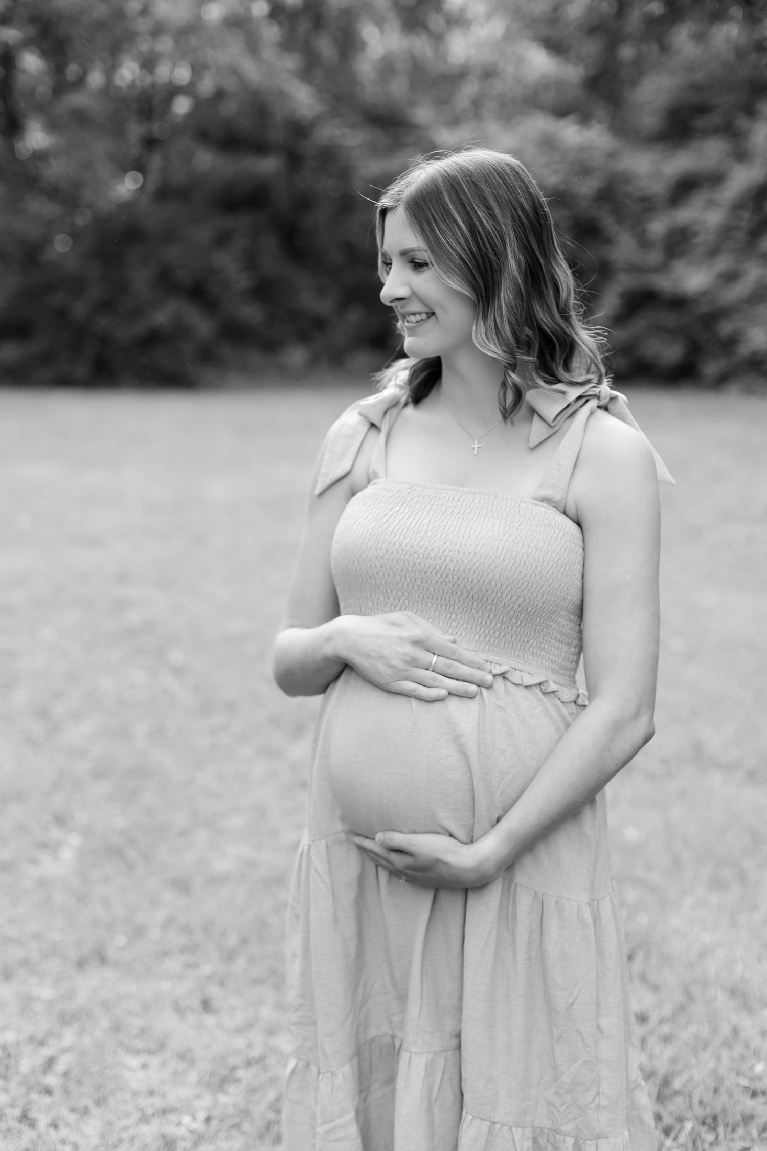 Black and white portrait of pregnant woman holding her baby bump in meadow.