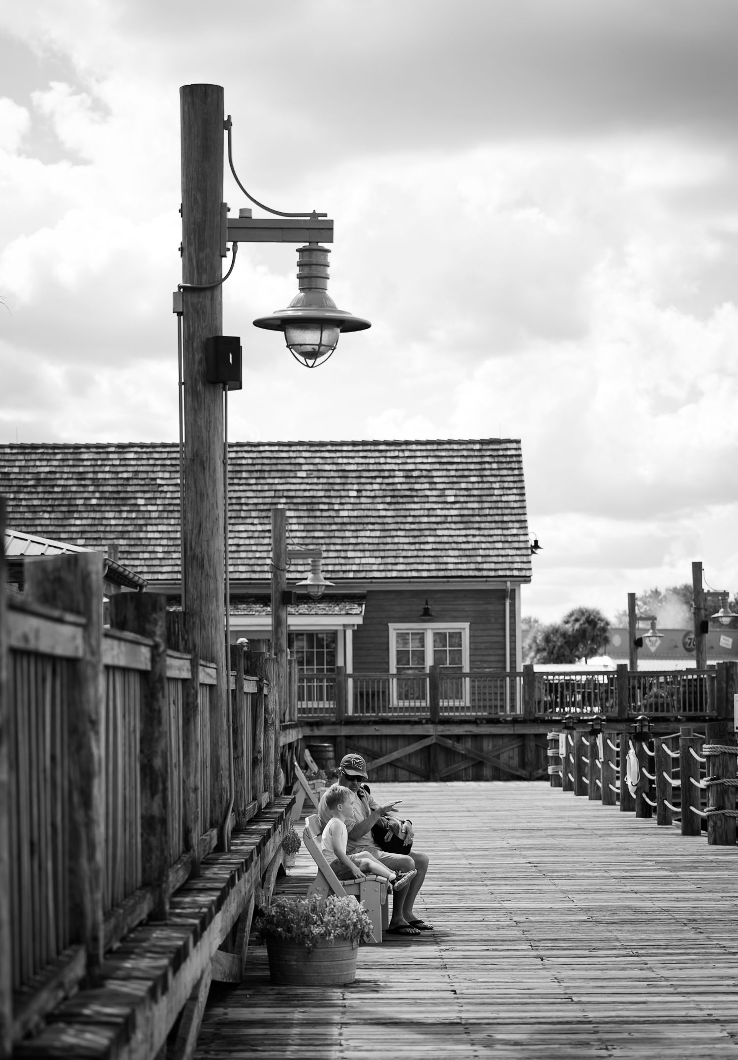 Black and white image of a grandfather and grandson sitting on a bench on a wooden boardwalk by Katy Rose Photography.