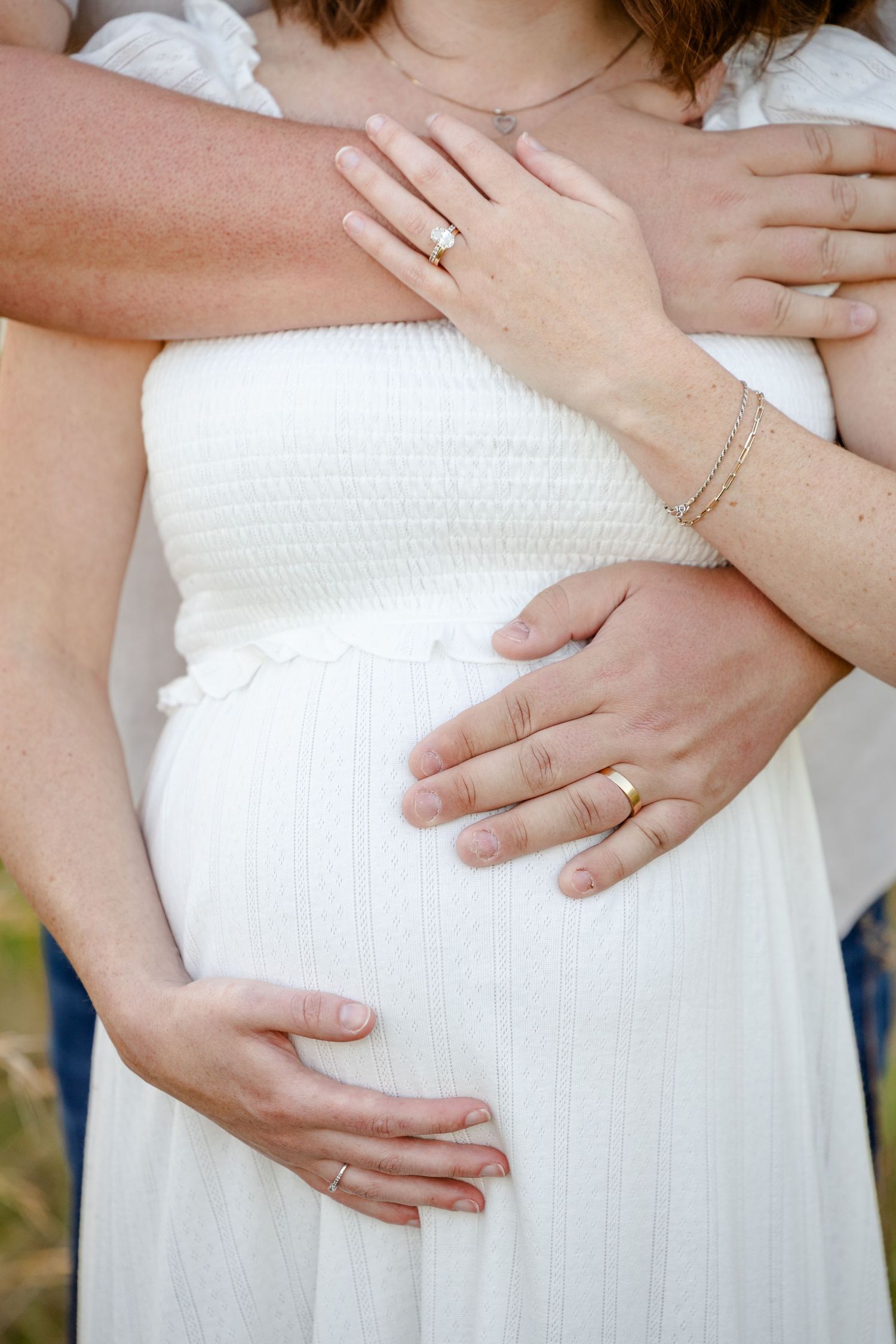 Close-up of couple's hands tenderly holding pregnant belly in white dress during Avon, Indiana maternity portraits by Katy Rose Photography
