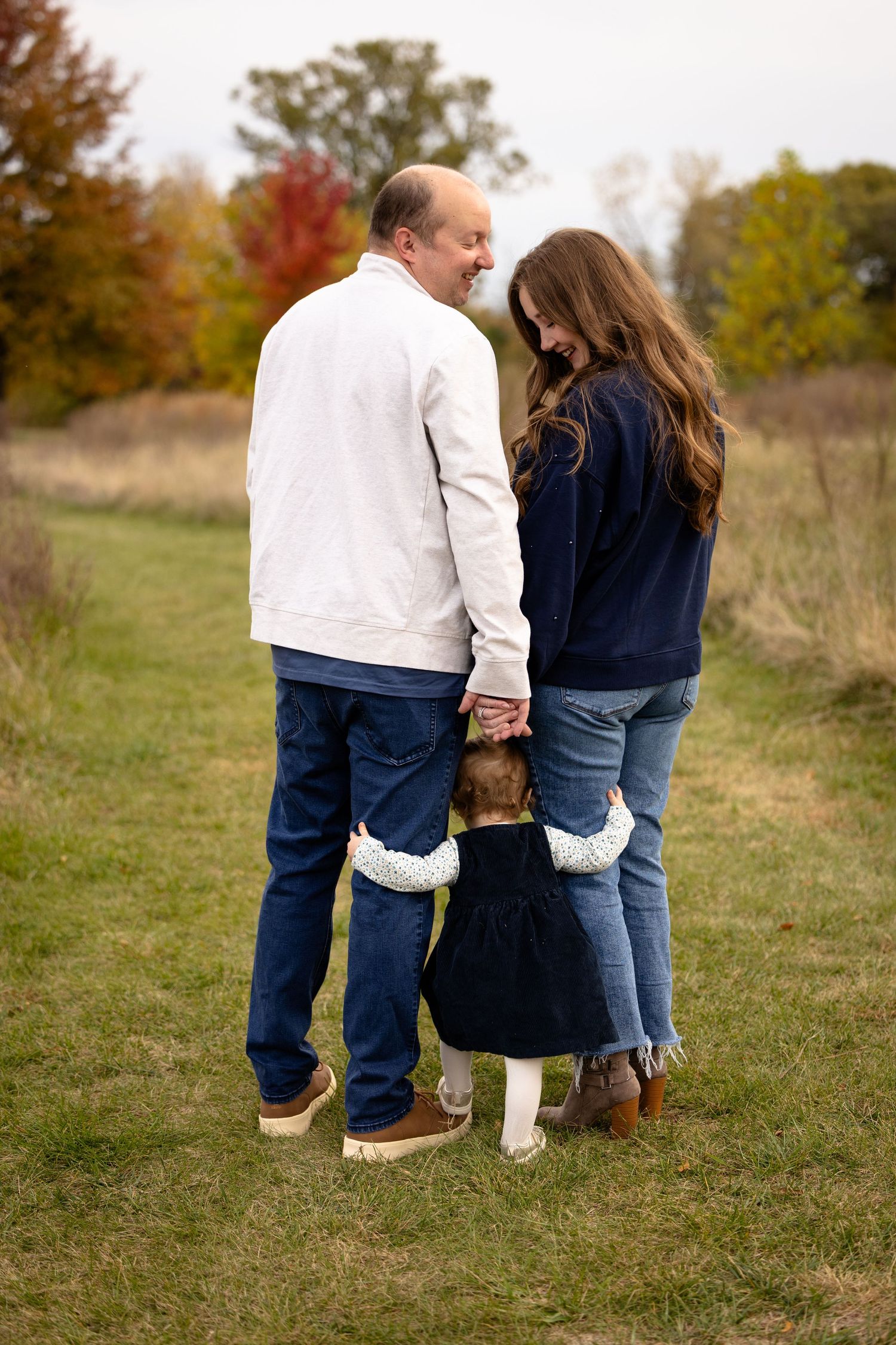 Back view of people standing together on grassy field in autumn during family photoshoot in Avon, Indiana.